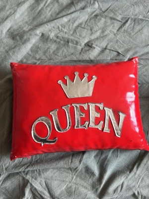 Röd clutch med QUEEN-tryck - Cool röd clutch i glansigt material med silverfärgad krona och texten 'QUEEN' på framsidan. Rektangulär form och enkel baksida utan detaljer. Perfekt accessoar för dig som vill sticka ut.