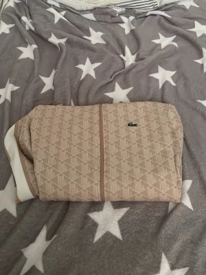 Beige zip-hoodie från Lacoste - Säljer en beige hoodie från Lacoste med dragkedja och diskret mönster över hela plagget. Klassisk krokodil-logga på bröstet och vita detaljer längs ärmarna. Ribbad mudd vid ärmslut och nederkant. Perfekt för en chill och stilren look.