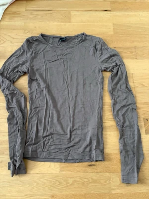Beige långärmad topp i bomull - En enkel och stilren beige långärmad topp med rund halsringning. Tillverkad i mjuk bomull och har en normal passform som funkar till många olika looks. Perfekt att styla med jeans eller kjol för en clean vibe. Den har även liten slita vid ärmarna 