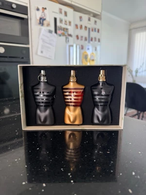 Jean Paul Gaultier Le Male parfymset - Snyggt parfymset från Jean Paul Gaultier med tre flaskor i form av manliga torsos. Två flaskor är mattsvarta med guldiga detaljer och en är guld med röda och blå ränder. Kommer i en stilren presentförpackning med konstnärlig design.