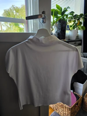 Vit croppad t-shirt - Säljer en enkel och stilren vit croppad t-shirt med korta ärmar och rund hals. Perfekt till jeans eller kjol för en clean look. Materialet känns mjukt och stretchigt, troligen bomull eller en bomullsblandning. Den är lite fläckig i kragen men det syns knappt när man har på sig den