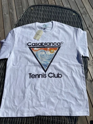 Vit Casablanca Tennis Club t-shirt - Snygg vit t-shirt från Casablanca med stort färgglatt tryck på bröstet och texten 'Tennis Club'. Klassisk passform och rund hals. Perfekt för dig som gillar sportig och trendig stil.