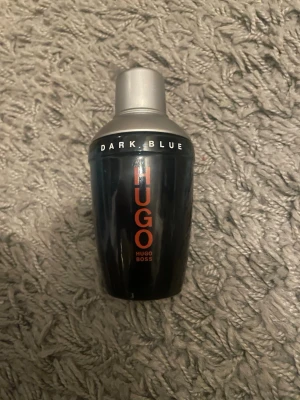 Hugo Boss Dark Blue parfym - Säljer en cool parfym från Hugo Boss, modellen Dark Blue. Flaskan är mörkblå med silverfärgat lock och har en modern, shaker-inspirerad form. Märkets logga syns tydligt i rött på framsidan. Perfekt för dig som gillar stilrena och maskulina dofter. Storlek 75 ml och skulle säga att det är runt 60-70 ml kvar