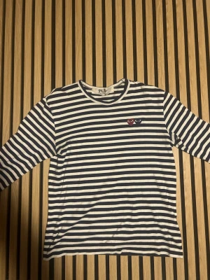 Randig långärmad t-shirt från Comme des Garçons Play - Snygg långärmad t-shirt från Comme des Garçons Play med marinblå och vita ränder. Bröstet pryds av två små hjärtan, ett rött och ett blått, med ögon. Klassisk rund halsringning och mjukt bomullsmaterial. Passar från personer som bär S till M. Ifall ni har fler frågor så svarar vi snabbt!