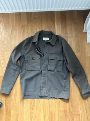 Oliv grön overshirt - Stilren grå overshirt från Legends med två stora bröstfickor med knappstängning och klassisk krage. Tillverkad i ett mjukt bomullstyg och har dragkedja framtill. Perfekt lager-på-lager-plagg för en avslappnad look.