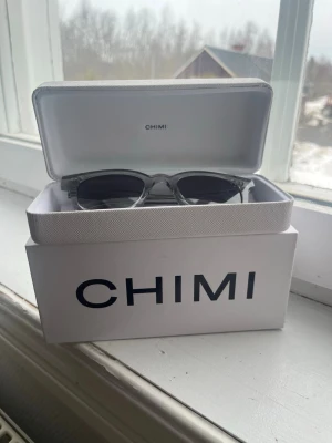 Chimi transparenta solglasögon - Snygga solglasögon från Chimi med transparent, tjock plastbåge och mörka, tonade glas. Klassisk rektangulär form som passar till många stilar. Kommer med originaletui och box.