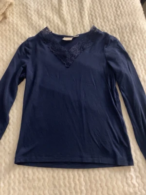 Marinblå långärmad topp från Gina Tricot - Storleken är XS. Snygg marinblå långärmad topp från Gina Tricot med spetsdetaljer vid v-ringad hals. Perfekt för dig som gillar stilrena plagg med en twist. Materialet är mjukt och bekvämt, och spetsen ger en extra touch. Passar till många olika outfits.