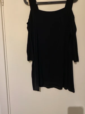 Svart offshoulder topp - Snygg svart offshoulder topp med breda axelband och trekvartsärm. Perfekt för dig som vill ha en stilren och trendig look. Passar till många olika outfits och är enkel att matcha.