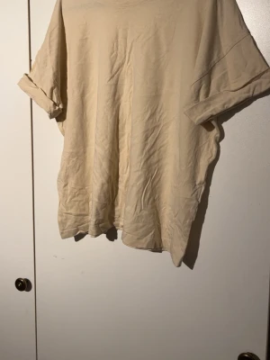 Beige oversized t-shirt - En enkel och stilren beige t-shirt med avslappnad oversized passform. T-shirten har korta ärmar som är uppvikta och är gjord i mjuk bomull. Perfekt för en chill och casual look.