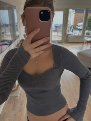 Mörkgrå ribbad långärmad topp - Säljer en mörkgrå ribbad topp med lång ärm och fyrkantig ringning. Toppen är figurnära och har en croppad passform som ger en modern look. 