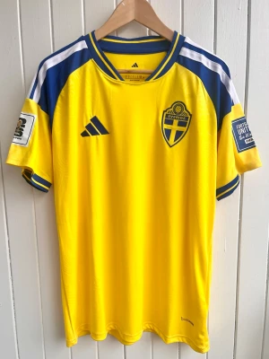 Sverige - Matchtröja 2026 - Fan version (L) - Säljer en svensk landslagströja 2026 (fan version). Tröjan är en reprint i nyskick. Inget namn eller nummer. WC-patches på ärmarna.    Storlek: Large