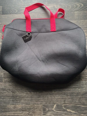 Grå weekendbag från Diesel - Snygg och rymlig weekendbag från Diesel i grått tyg med diskret mönster och starka rosa handtag. Väskan har en metallbricka med Diesel Parfums-logga och är perfekt för resor eller gymmet. Praktisk och trendig design som sticker ut.