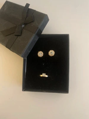 Guldtonade örhängen med stenar - Säljer ett par eleganta örhängen i guldton med gnistrande, runda stenar i mitten. Örhängena har en klassisk och tidlös design som verkligen fångar ljuset. Perfekta för dig som gillar stilrena accessoarer med lite extra bling.