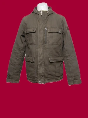 Field jacka  - Snygg olivgrön parkas med huva och dragkedja framtill. Jackan har flera praktiska fickor med lock och knapp, samt en bröstficka med dragkedja. Justerbara muddar vid ärmslut och dragsko i huvan. Perfekt för kyliga dagar.