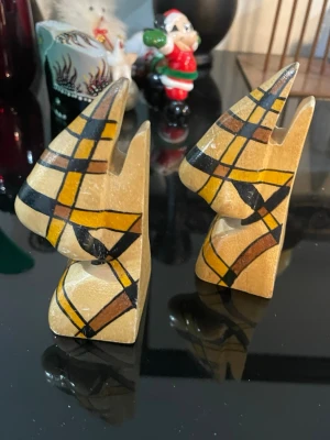 Afrikanska bokstöd i trä - Säljer ett par handgjorda bokstöd i trä med abstrakt design i gult, svart och brunt. Bokstöden har geometriska mönster och är formade som stiliserade djurhuvuden. Perfekt som unik inredningsdetalj till bokhyllan.