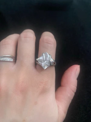Silverring med stor klar sten - Snygg silverfärgad ring med en stor, klar sten i mitten. Ringen har en elegant och klassisk design med öppna detaljer runt stenen som ger ett lyxigt intryck. Perfekt för dig som gillar statement-smycken och vill sticka ut.