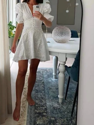Adoore sicely dress - Söt vit kortklänning med puffärmar och v-ringning. Klänningen har markerad midja och lätt utställd kjol, samt fina broderade detaljer i tyget. Perfekt för sommarens alla tillfällen. Perfekt till student 