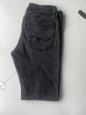 Grå jeans från Jack and jones - Snygga grå jeans från Jack and Jones  med klassisk femficksdesign och svarta sömmar. Jeansen har en rak passform och är tillverkade i mjukt denimtyg. Perfekta för en avslappnad och stilren look. Skicket är super och de är storlek 32 34