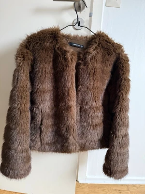 Brun fuskpälsjacka från Gina Tricot - Säljer en fluffig brun fuskpälsjacka från Gina Tricot. Jackan har rund halsringning, långa ärmar och är helfodrad för extra värme. Perfekt för dig som vill ha en trendig look. Ny pris 599