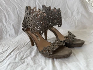 Greige pumps med stenar/diamanter i metall - Snygga gråa pumps med klack och unika utskurna detaljer i blommönster. Skorna har öppna tår och dekoreras med små nitar för extra edge. Perfekta för dig som vill sticka ut med din stil. Märke Alma en Pena. Skicket är mkt fint utom synliga märke på undersidan av sulan 