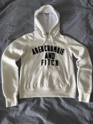 Abercrombie & Fitch hoodie - Snygg och skön vit hoodie med texten Abercrombie and Fitch. Knappt använd och mycket bra kvalitet. Tröjan är i storlek M men den är mycket liten och passar som en XS, skriv för mått. Hör av dig om du har frågor, pris kan diskuteras!