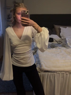 Vit omlottblus med vida ärmar - Snygg vit omlottblus med djup V-ringning och långa, vida ärmar. Blusen har figurnära passform med rynkade detaljer i sidan. Säljer den för har aldrig använt den och prislappen sitter kvar! Stolek Xs nypris 399, säljer för 300❤️