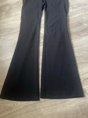 Svarta utsvängda kostymbyxor - Snygga svarta kostymbyxor med utsvängda ben och diskreta bakfickor. Byxorna har en klassisk look och är tillverkade i ett mjukt tyg som ger en skön känsla. Perfekta för dig som gillar en trendig siluett med lite extra attityd. För korta för mig som är 177cm