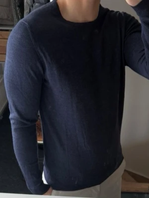 Mörkblå stickad tröja J.Lindeberg - Mörkblå stickad tröja från J.Lindeberg med rund halsringning och lång ärm. Tröjan har en stilren och enkel design, perfekt för lager på lager. 100% merinoull storlek m men sitter som xs