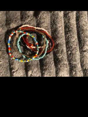 Färgglada pärlarmband i mixade färger - Säljer flera handgjorda armband med små pärlor i olika färger som blått, rött, vitt, gult och turkost. Armbanden är elastiska och har en bohemisk vibe, perfekta för att mixa och matcha. Materialet är plastpärlor i olika former och färger.
