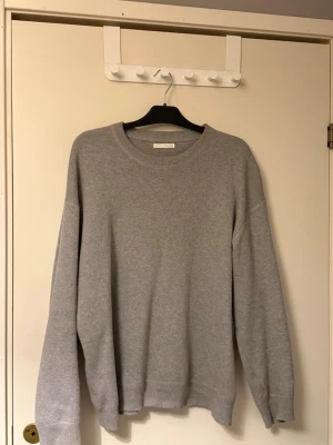 Grå stickad tröja ZARA - En enkel och stilren grå stickad tröja från Arket med rund halsringning och långa ärmar. Tröjan har ribbade muddar vid ärmslut och nederkant, perfekt för lager på lager och en clean look. Materialet är mjukt och behagligt.