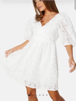 Studentklänning - Vit kort klänning med v-ringning och puffärmar. Helt oanvänd och med prislappen kvar. Storlek XS, 32/34 men väldigt stor i storleken. Köpt för 799. 