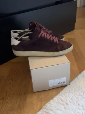 Vinröda Saint Laurent sneakers i mocka - Snygga vinröda sneakers i mocka med matchande vinröda skosnören och vit sula. Hälpartiet är vitt vilket ger en schysst kontrast. Perfekta för dig som gillar stilrena och klassiska sneakers med en twist. Passar till det mesta och är riktigt bekväma. Säljer eftersom dom tyvärr har blivit för små. Nypris 5000 mitt pris 1700