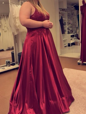 Vinröd långklänning i satin - Elegant vinröd balklänning i glansigt satinmaterial med spetsdetaljer upptill och v-ringad urringning. Klänningen har axelbandslös design och ett svepande långt kjolparti som ger en lyxig känsla. Perfekt för bal eller festliga tillfällen. Köpte klänningen för 8000kr på högtidshuset i Borlänge, underkjol kan fås med för 200kr till