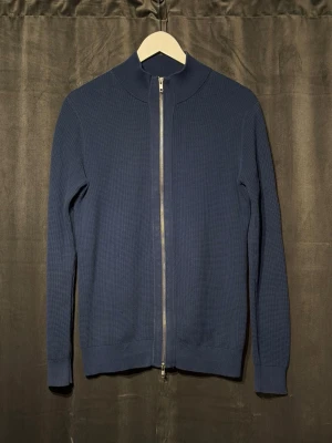 John Henric ziptröja  - Mörkblå stickad tröja med hel dragkedja ifrån John Henric.. Tröjan har en diskret, stilren design. Perfekt för lager på lager och enkel att matcha.
