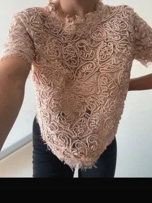 Beige spetsblus med dragkedja - Säljer en superfin beige spetsblus med korta ärmar och snygg dragkedja i ryggen. Blusen har vackra spetsdetaljer och är lätt transparent, perfekt för att lyfta din outfit. Passar dig som gillar romantisk och trendig stil.