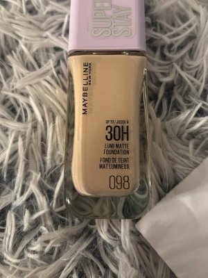 Maybelline Super Stay Foundation 098 - Maybelline Super Stay 30H Lumi-Matte Foundation i nyansen 098. Kommer i en rektangulär glasflaska med ljuslila plastlock. Ger en matt finish och håller länge. Perfekt för dig som vill ha en naturlig look med bra täckning.