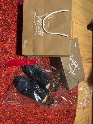Svarta sneakers från Christian Louboutin - Snygga svarta sneakers från Christian Louboutin med klassisk röd sula och diskret logga. Skorna har en låg silhuett, snörning och är tillverkade i mocka och läder. Perfekta för dig som vill ha en exklusiv och stilren look.