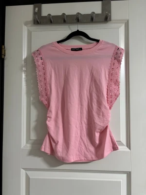 Rosa topp med spetsdetaljer  - Söt ljusrosa topp. Med spetsdetaljer längs ärmarna. Toppen är ärmlös och har en rund halsringning. Perfekt för vår och sommar. Enkel men ändå stylish design som passar till mycket.