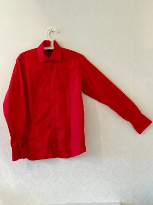 Röd slim fit skjorta från Dressmann - Snygg röd skjorta från Dressmann i slim fit-modell. Skjortan har klassisk krage, långa ärmar och knäppning framtill. Perfekt för dig som vill sticka ut med en färgstark look. Tillverkad i mjuk bomull för skön känsla.