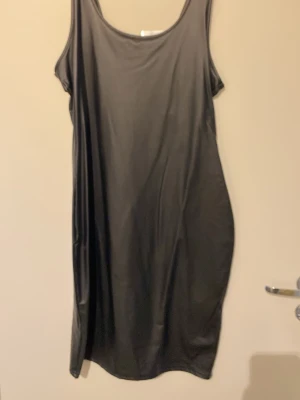 Svart ärmlös klänning - En enkel svart klänning med rund halsringning och ärmlös design. Klänningen har en figursydd passform och är tillverkad i ett mjukt, lätt material som ger ett snyggt fall. Perfekt att styla med accessoarer för en personlig look.