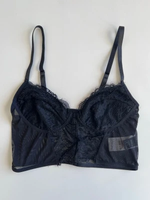 Svart spets-bh bralette, stl XS - Svart bralette med spets och tunna, justerbara axelband. Ingen bygel och inga ilägg. Perfekt för dig som gillar en feminin och stilren look. Fin blandning mellan mesh- och spetsdetaljer.