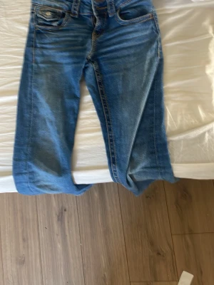 Två par raka blå jeans - Säljer två par klassiska blå jeans i olika tvättar, båda med raka ben och femficksmodell. Jeansen har normal midja och är tillverkade i denim med snygga kontrastsömmar. Perfekta för en avslappnad och trendig look.