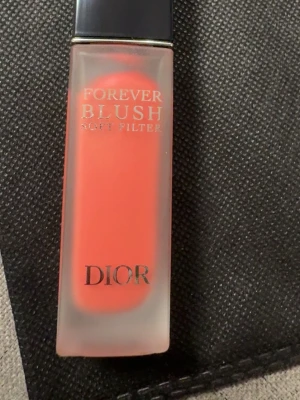 Dior Forever Blush Soft Filter 03 Bloom - Flytande rouge från Dior i nyansen 03 Bloom. Kommer i en frostad glasflaska med svart lock. Färgen är en livlig korallrosa som ger kinderna en fräsch och naturlig look. Perfekt för att skapa en mjuk och jämn finish.