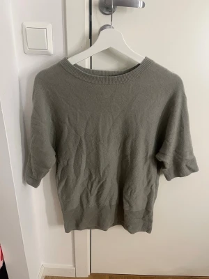 Grön cashmere tröja från H&M - Mjuk och stilren grön stickad tröja från H&M i kashmir. Tröjan har korta ärmar, rund halsringning och ribbade kanter. Perfekt för dig som gillar minimalistisk och bekväm stil.