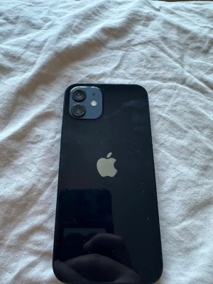 Mörkblå Iphone 12 - Snygg svart iPhone 12 med stilren design och två kameror på baksidan. Telefonen har en platt ram i aluminium och baksida i glas med den klassiska Apple-loggan. Perfekt för dig som gillar modern och minimalistisk look. pris kan diskuteras 