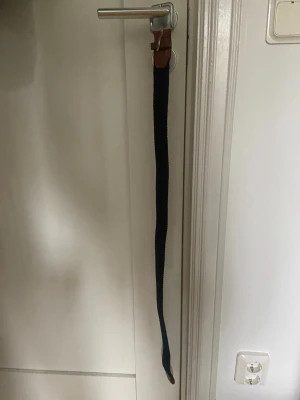 Mörkblått bälte från Jack & Jones - Snyggt mörkblått bälte från Jack & Jones med detaljer i brunt skinn. Bältet har en klassisk design med silverfärgat spänne och passar perfekt till jeans eller chinos.