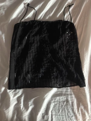 Svart glittrig linnetopp med paljetter - Säljer en svart glittrig linnetopp med tunna axelband och paljettdetaljer som ger ett extra lyft. 