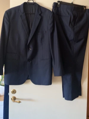 Mörkblå kostym  - Snygg mörkblå kostym med klassisk kavaj och matchande byxor. Kavajen har två knappar, smala slag och flera fickor. Perfekt för dig som vill ha en stilren och tidlös look. Materialet känns mjukt och följsamt. Mått kan ges efter önskemål 