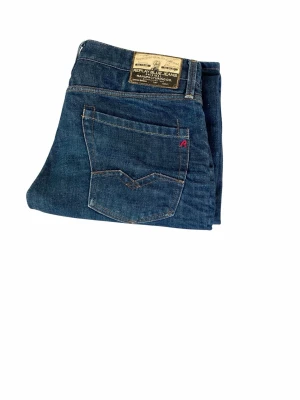 Blå jeans från Replay - Snygga blå jeans från Replay med klassisk femficksdesign och en tydlig läderpatch bak i midjan. Jeansen har raka ben och är gjorda i slitstarkt denim med kontrastsömmar. Perfekta för en avslappnad och trendig look.