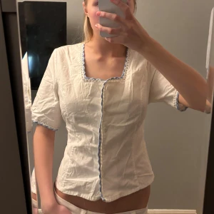 Vit blus med spetsdetaljer - Söt vit blus med korta ärmar och blå spetsdetaljer längs kanterna. Blusen är i storlek 38, jag har storlek S och den passar mig. 